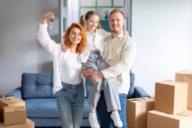Aile konutları. Mutlu ebeveynler ve kızlar ev anahtarlarını tutuyor, taşınma gününü kutluyor ve kameraya gülümsüyor.