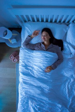 Geceleri yatakta uyuyan bir kadın, battaniyenin altına uzanmış, güzel rüyalar görüyor, dikey çekim yapıyor.