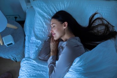 Serene genç kadın geceleri beyaz çarşaflarla yatağında uyuyor, tatlı rüyalar görüyor, manzaranın tadını çıkarıyor. Sakin atmosfer