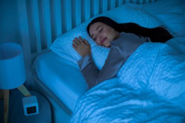 Sakin, mutlu bir kadın karanlık bir gece odasında yatak odasına uzanıyor, rahat bir yatakta uyuyor ve gülümsüyor.