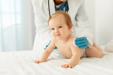 Çocuk aşılama konsepti. Kauçuk koruyucu eldivenli doktor klinikte aşı yaptıktan sonra bebek omzuna pamuk koyuyor.