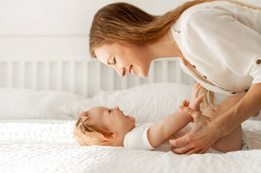 Mutlu anne yatak odasında küçük kızıyla oynuyor, kadın evde çocukla sabah rutininin keyfini çıkarıyor, yan görüş, boş alan.