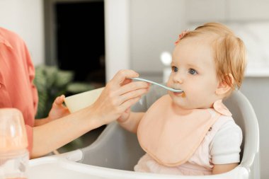 Anne çocuğu sebze yemeği için beslerken bebek sandalyeye oturup harmanlanmış yemek yiyor. Bebek insanlar için sağlıklı beslenme