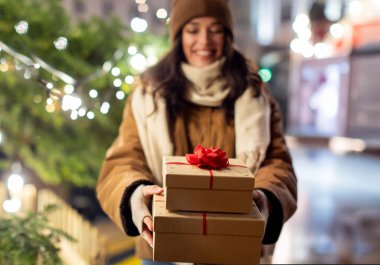 Kış tatili ve kutlama konsepti. Mutlu, gülümseyen bir kadının hediye kutularını açık havada Noel ışıklarının üzerine koyması.