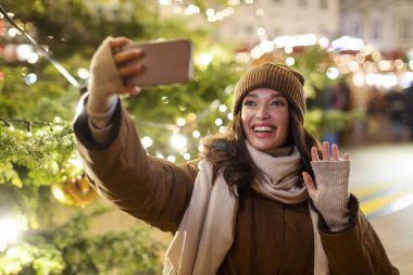 Mutlu Avrupalı bir kadının selfie çekerken portresi ya da açık hava görüntüsü çekerken Noel festivali atmosferini gösteriyor.