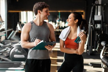 Spor salonunda kişisel antrenörüyle konuşan mutlu bir bayan. Antrenmandan sonra ya da teneffüste elinde su şişesi tutan bir kadın.