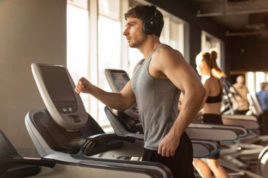 Spor salonunda koşu bandında koşarken kulaklıkla müzik dinleyen yakışıklı bir adam.
