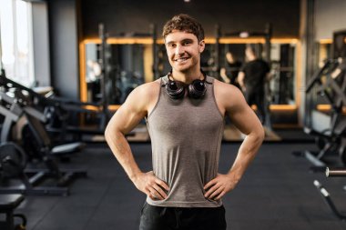 Modern spor kulübünün içinde duran, kameraya gülümseyen, sağlıklı yaşam tarzı ve spor reklamları yapan yakışıklı Avrupalı genç kaslı adamın portresi.