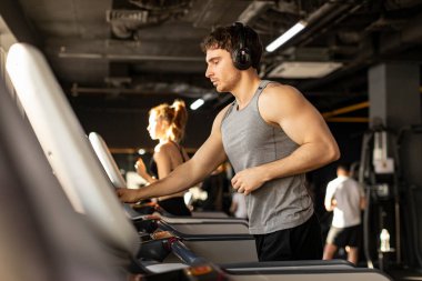 Avrupalı sporcu koşu bandında koşarken, spor yaparken ve iç mekanda müzik dinlerken hızı ayarlıyor