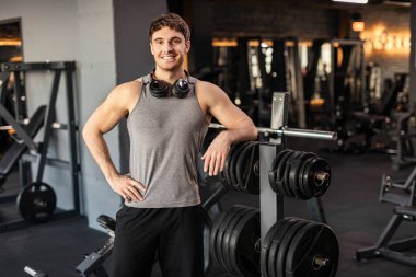 Sağlıklı bir yaşam tarzı. Güçlü adam gülümsüyor, kendinden emin erkek fitness antrenörü modern spor kulübünün içinde duruyor.