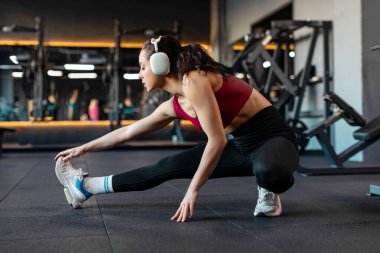 Sporcu genç bayan ısınıyor ve bacaklarını esnetiyor modern spor salonunda çalışırken, yan bakış açısıyla