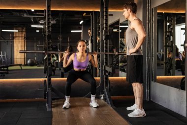 Fit bayan halterle egzersiz yaparken erkek antrenör spor salonunda kadın antrenmanı yapıyor.