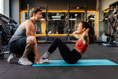 Formda genç bir kadın spor salonunda spor salonunda antrenörle antrenman yapıyor. Spor salonunda karın kasları çalışıyor.