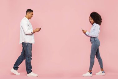 Siyah adam ve kadın cep telefonu ve mesaj kullanıyor, pembe stüdyo arka planında yürüyor, tam boy. Yeni mobil uygulama reklamı