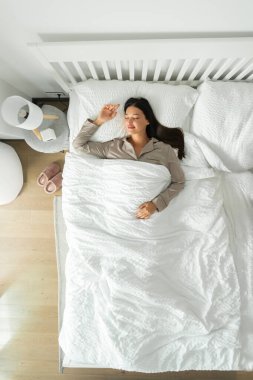 Beyaz çarşafların üzerine uzanmış, yatakta kestiriyor, battaniyenin altında uyuyor, dikey çekim yapıyor. Yenileme, enerji konseptini yenileme