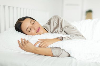 Huzurlu genç bir kadın uyuyor, yatakta uzanıyor, yastık ve battaniyeye sarılıyor, güzel rüyalar görüyor. Sağlıklı uyku konsepti