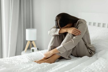 Evde pijamalı üzgün bir kadın, dizlerini kucaklıyor ve ağlıyor, kötü günler geçiriyor, yalnızlık çekiyor, boş bir alan.