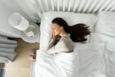 Huzurlu kadın rahat yatağında huzur içinde uyuyor, el ele tutuşuyor, battaniyenin altında uzanıyor ve rüyaların tadını çıkarıyor.