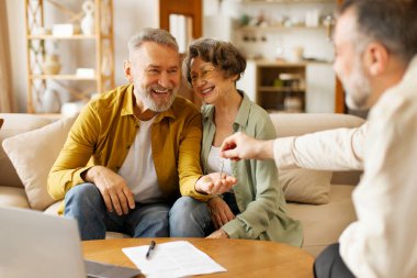 Ajanın yeni evden heyecan içindeki yaşlı eşlere anahtar vermesi, kendi mülkünü satın alması, içeride kanepede oturması. Ev satın alma ve kira kavramı