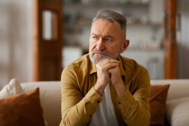 Düşünceli sakallı son sınıf öğrencisi yalnız başına koltukta oturuyor, kendini yalnız ve üzgün hissediyor.
