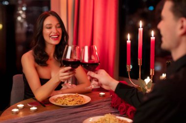 Romantik bir akşam yemeği. Mutlu çift kadeh tokuşturuyor, Sevgililer Günü 'nde akşam yemeğinin tadını çıkarıyor, aşkı ve kutlamayı simgeliyor.