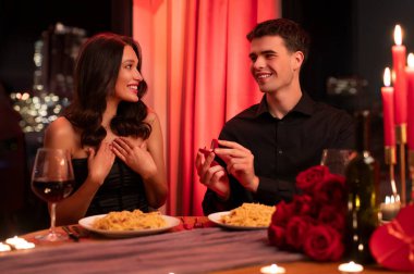 Neşeli bir adam sürpriz bir bayana nişan yüzüğü veriyor, romantik bir ortamda oturuyor, Sevgililer Günü 'nü kutluyor.