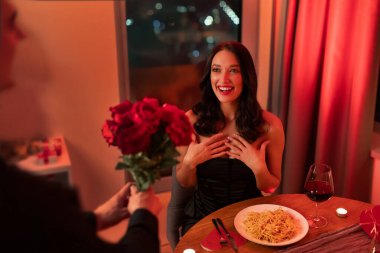 Romantik sürpriz. Akşam restoranda akşam yemeğinde mutlu bayana kırmızı güller veren bir adam, Sevgililer Günü 'nü birlikte kutluyor.