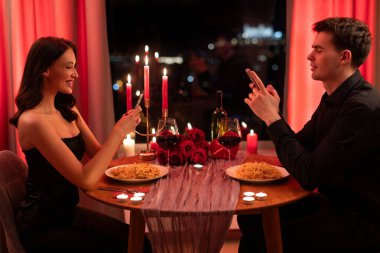 Online flört uygulaması. Restoranda romantik bir akşam yemeği sırasında cep telefonu kullanan genç bir adam ve kadın masada oturup birbirlerini görmezden geliyorlar.