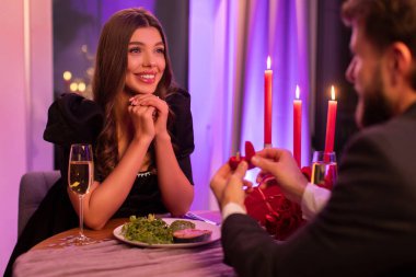 Adam mutlu bir bayana nişan yüzüğü veriyor, restoranda romantik bir ortamda oturuyor, Sevgililer Günü 'nü kutluyor.