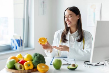 Çekici Avrupalı beslenme danışmanı elinde turuncu tutuyor ve danışmanlık yapıyor, müşteriler için yemek planı yapıyor, kilo verme kliniğinde çalışıyor.