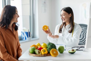 Kadın hastalarla çalışan mutlu diyetisyen doktor, meyve ve sebze yemenin, ofiste danışmanlık yapmanın önemini bir kadınla konuşuyor.
