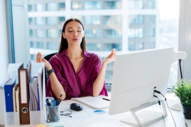 İşte stresle başa çıkmak. Ofiste meditasyon yapan kadın ofis çalışanı, kapalı gözlerle nefes alma egzersizleri yapıyor.