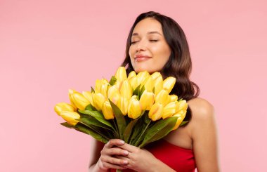 Mutlu bayanın lale buketini koklaması, çiçek aromasının tadını çıkarması, pembe arka planda izole edilmiş mutlu bahar tatili.