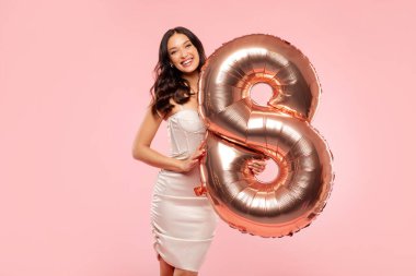 8 numaralı balonu tutan ve kameraya gülümseyen mutlu genç bayan, Pembe stüdyo arka planında poz veren kadın gününün tadını çıkar.