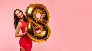 8 Mart kutlamaları. Kadınlar Günü için elinde 8 numaralı altın balon olan güzel bir kadın pembe stüdyo arka planında poz veriyor.