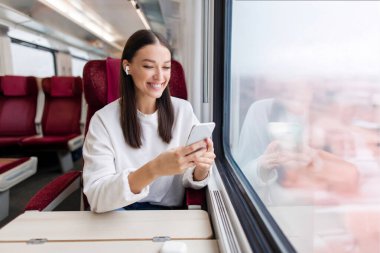 Trenle seyahat eden, akıllı telefon kullanan, video izleyen ya da müzik dinleyen mutlu, güzel kadın turistin tatili başlıyor.