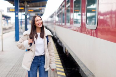 Tren istasyonunun peronunda Avrupalı bir kadın yolcu, trenin yanında duruyor, arabasını arıyor, hafta sonu gezisi için hazır.