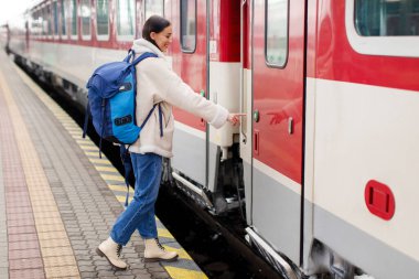 Kadın turist, tren kapısında girmek için düğmeye basıyor, kadın ceketli ve sırt çantalı, hafta sonu tatiline hazır. Demiryolu konsepti