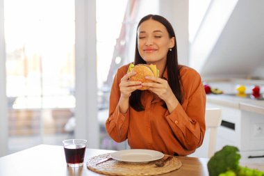 Heyecanlı bir kadın taze hamburgerin kokusundan zevk alıyor. Hamburger ve kolayla aldatıyor. Mutfakta bedava yer var.