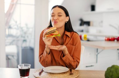 Fast food. Heyecanlı bayan lezzetli ev yapımı hamburgerleri seviyor, evde abur cubur yiyor, mutfağın içinde oturuyor, bedava yer var.
