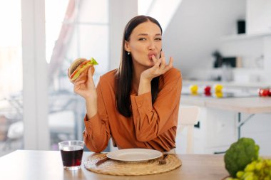 Tatli ev yapimi hamburgerleri yerken parmaklarini yalayan, abur cuburdan zevk alan ve evde yemegi aldatan bir kadin.