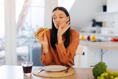 Hile yemeği. Mutlu kadın lezzetli hamburgerleri yemekten ve parmaklarını yalamaktan zevk alır.