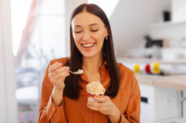 Eğlence ve tatlılar. Mutlu bayan dondurma yiyor ve gülümsüyor, mutfağın içinde oturuyor, tatlıya zaman ayırıyor.