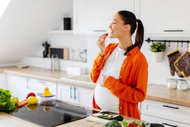 Mutfak içinde salata pişirirken koca göbekli, organik sebze yiyen tatmin olmuş hamile kadın. Diyet, evde sağlık hizmeti, çocuk beklentisi, tat alma isteği.