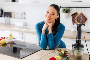 Beslenme konsepti. Fitness antrenmanından sonra güzel fit bayanın portresi, masaüstüne yaslanıp taze yemek yemek, modern mutfakta poz vermek. Sağlıklı beslenme ve beslenme