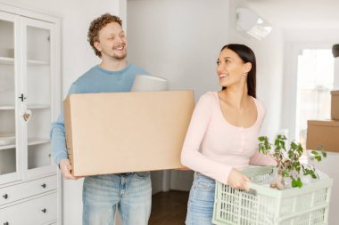 Heyecanlı, sevgi dolu bir çift yeni bir daireye taşınıyor. Eşyalarıyla birlikte duruyorlar ve birbirlerine gülümsüyorlar. Taşınma, taşınma, emlak konsepti