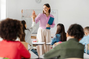 Gülümseyen genç bayan öğretmen son okul dersinden sonra öğrencilerine beşlik çakıyor. Eğitim, öğretim, öğrenme ve öğrenim yılı konsepti