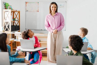 Öğretmenlerini dikkatle dinleyen öğrenciler, ders sırasında dizüstü bilgisayarlarıyla masalarında oturup, destekleyici öğrenme ortamı gösteriyorlar.