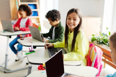 Derste dizüstü bilgisayarla oturan mutlu öğrenci, modern sınıfta sınıf arkadaşlarıyla internetten öğreniyor. Teknoloji ve eğitim kavramı