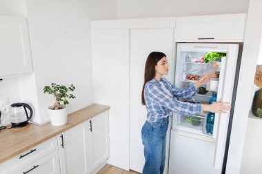 Genç bir bayanın buzdolabından ürünleri çıkarması, evde ne pişireceği, mutfağın içi, boş alan planlaması.